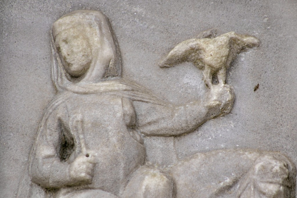 La figura femminile procede a cavallo, mentre regge un frustino e un falcone.